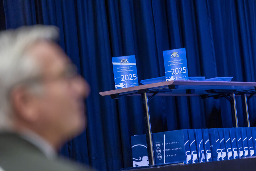 Blauer Vorhang, Tisch mit blauen Ordnern und Schildern "2025", unscharfe Person im Vordergrund.