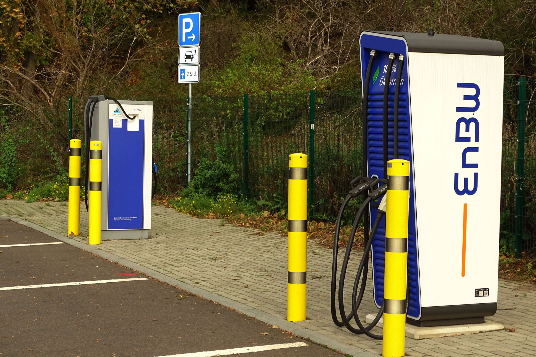 Ladestation für Elektroautos mit gelben Pollern und Parkplatzschild im Hintergrund.