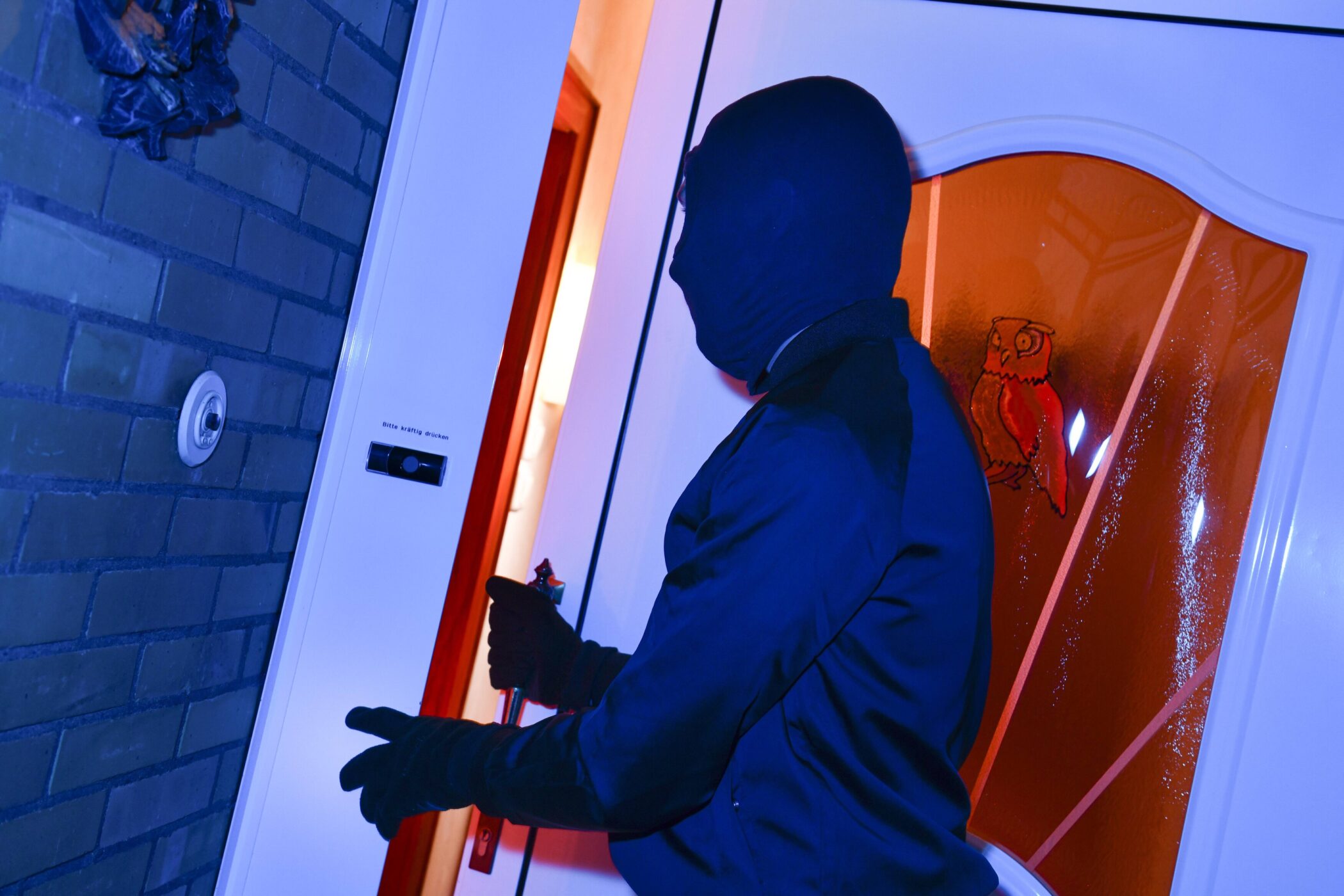 Person in dunkler Kleidung öffnet eine Tür mit einem Werkzeug.