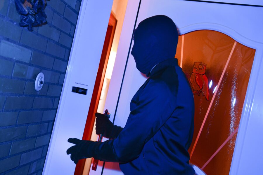 Person in dunkler Kleidung öffnet eine Tür mit einem Werkzeug.