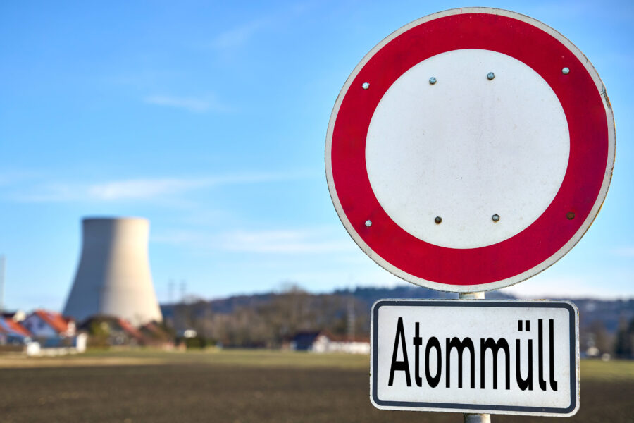 Verkehrsschild mit Aufschrift "Atommüll", Kühlturm im Hintergrund.