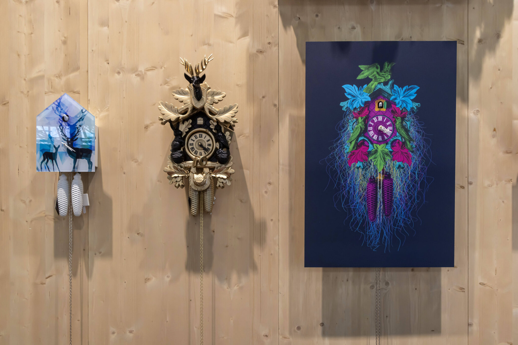 Drei Kuckucksuhren an einer Holzwand, mittlere Uhr mit Hirschkopf.