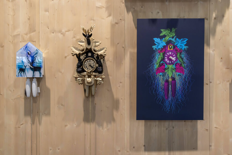 Drei Kuckucksuhren an einer Holzwand, mittlere Uhr mit Hirschkopf.