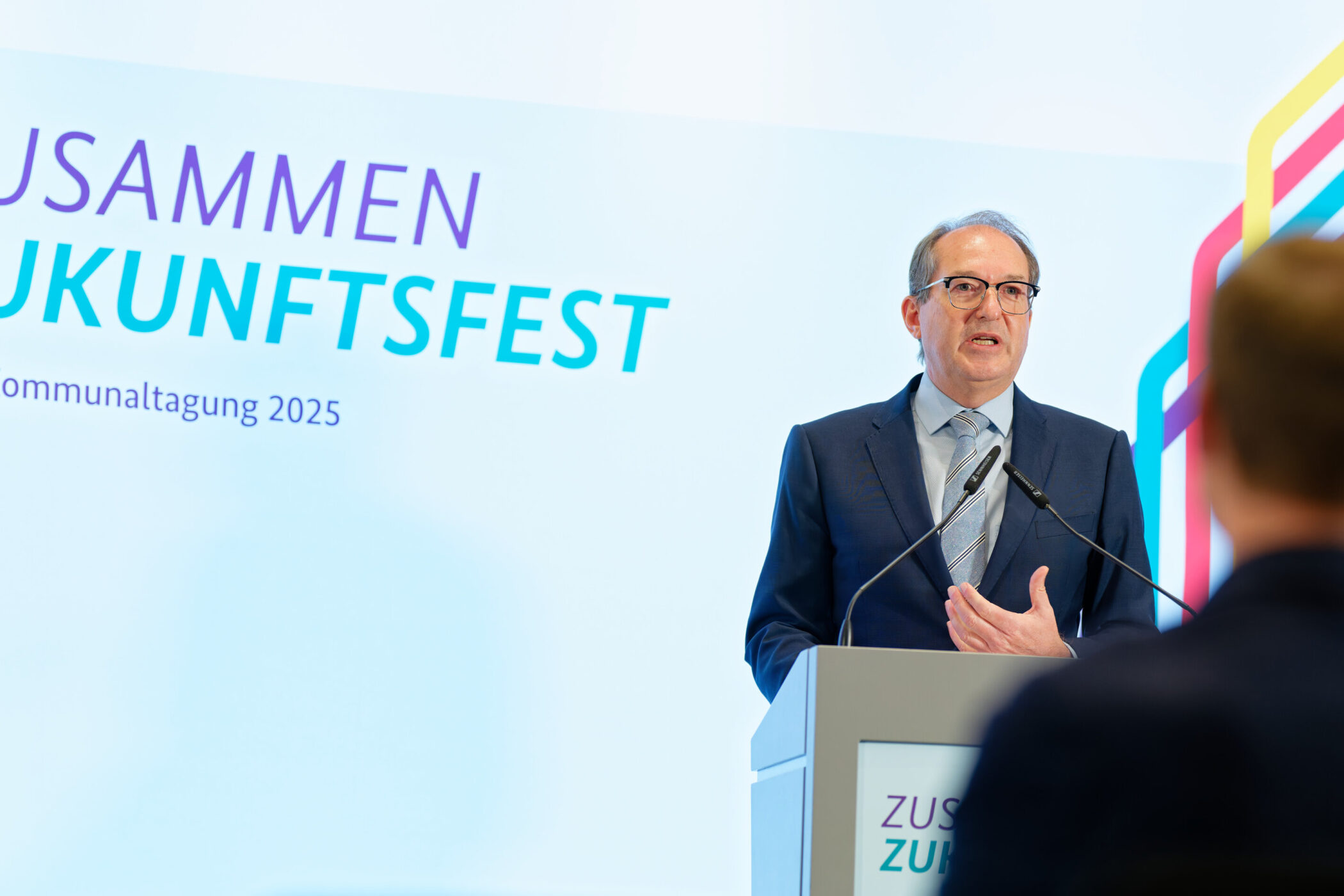 Mann am Rednerpult, Hintergrundtext: "ZUSAMMEN ZUKUNFTSFEST, BMI-Kommunaltagung 2025".