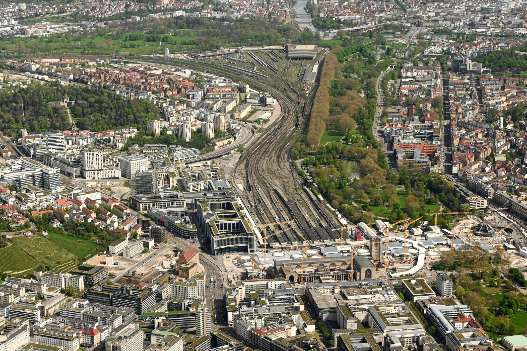 Luftaufnahme einer Stadt mit Bahngleisen, Gebäuden und Grünflächen.
