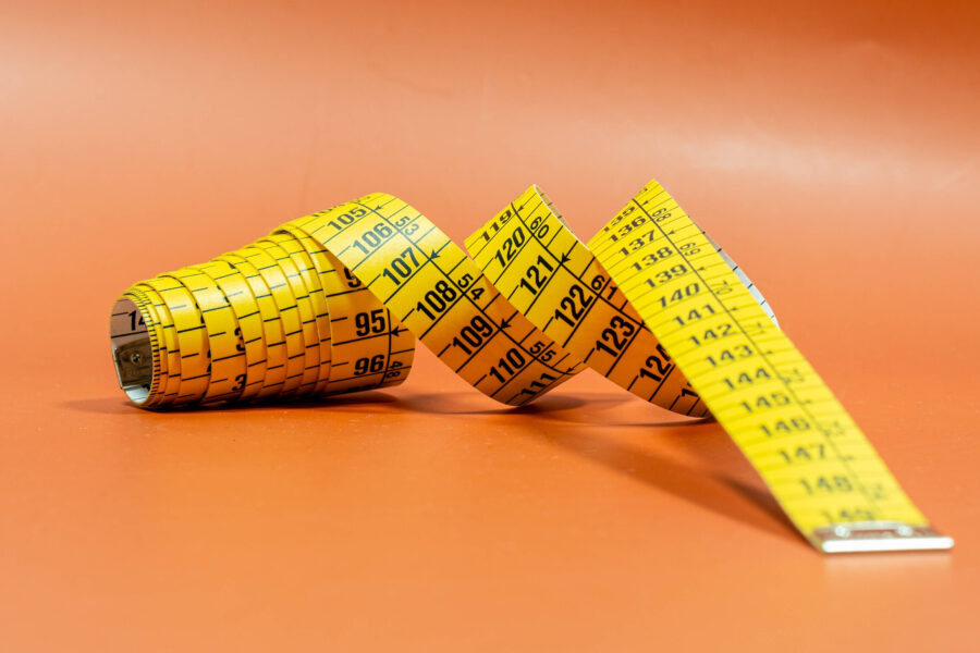 Gelbes Maßband auf orangefarbenem Hintergrund, teilweise ausgerollt.