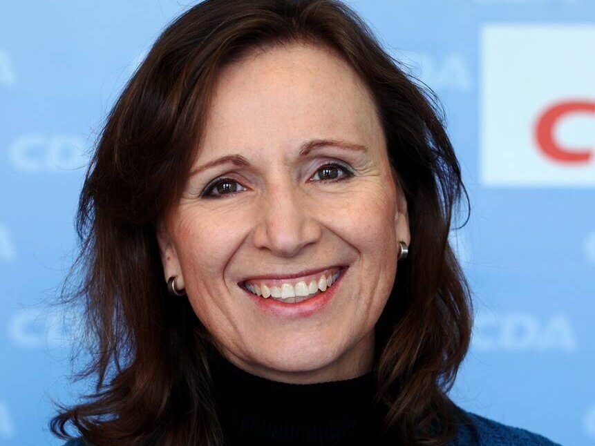 Frau lächelt vor blauem Hintergrund mit CDA-Logo.