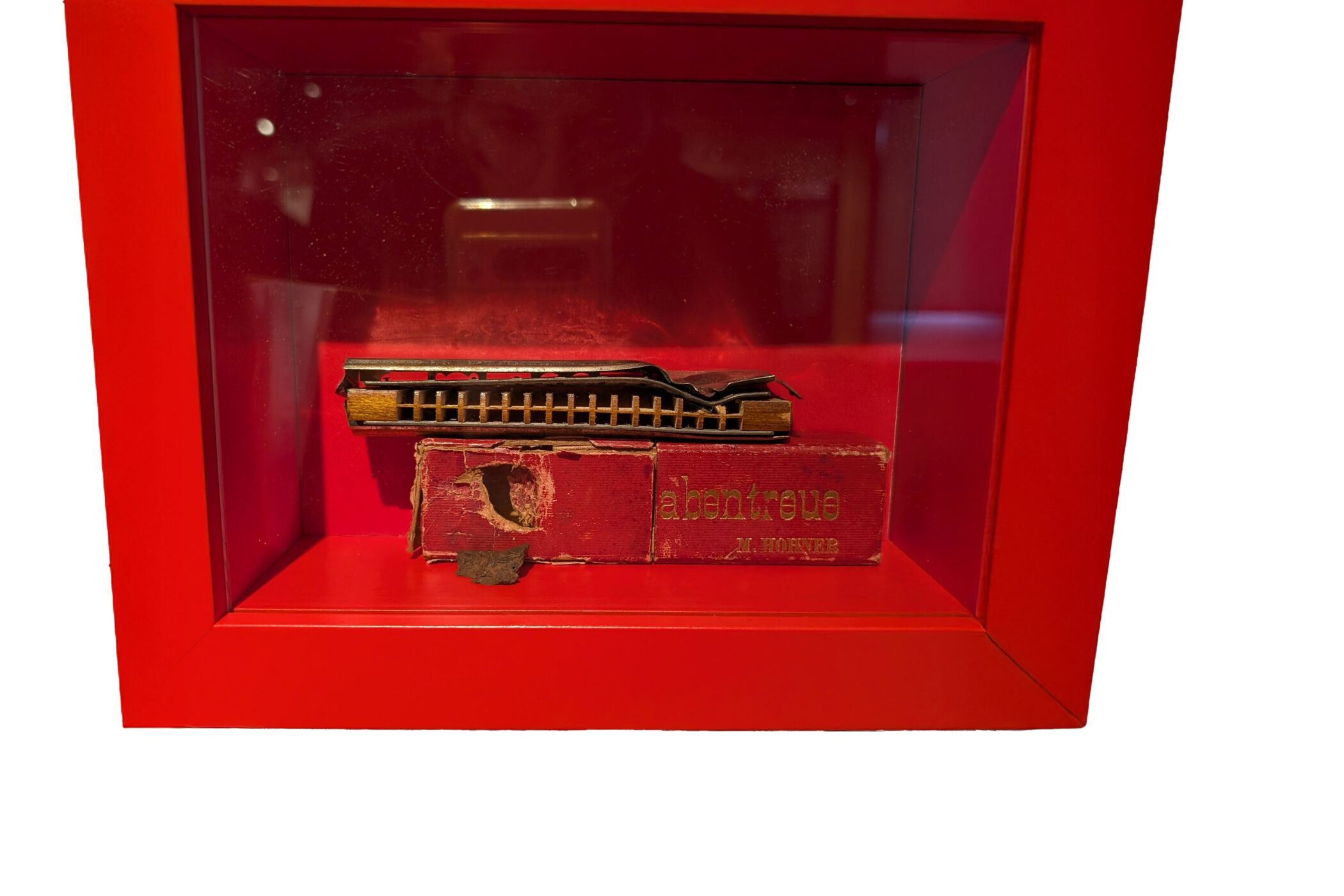 Rote Box mit Mundharmonika und abgenutzter Verpackung.