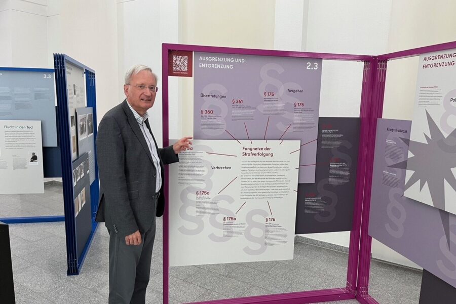 Älterer Mann zeigt auf eine Ausstellungstafel mit Texten und Paragraphen.