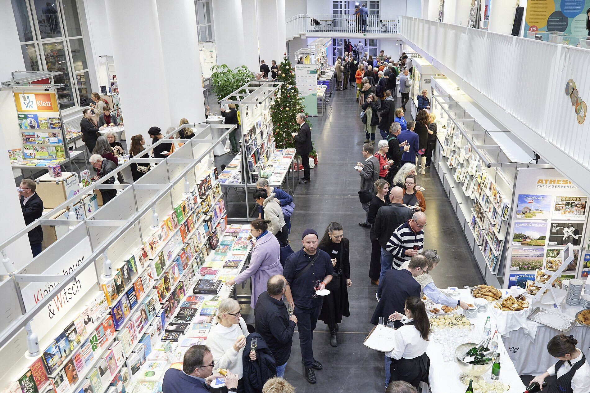 Menschenmenge in einer Buchmessehalle mit Ständen und Büchern.