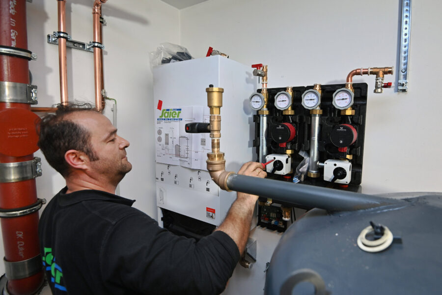 Ein Mann arbeitet an einer Heizungsanlage mit Rohren und Druckanzeigen.