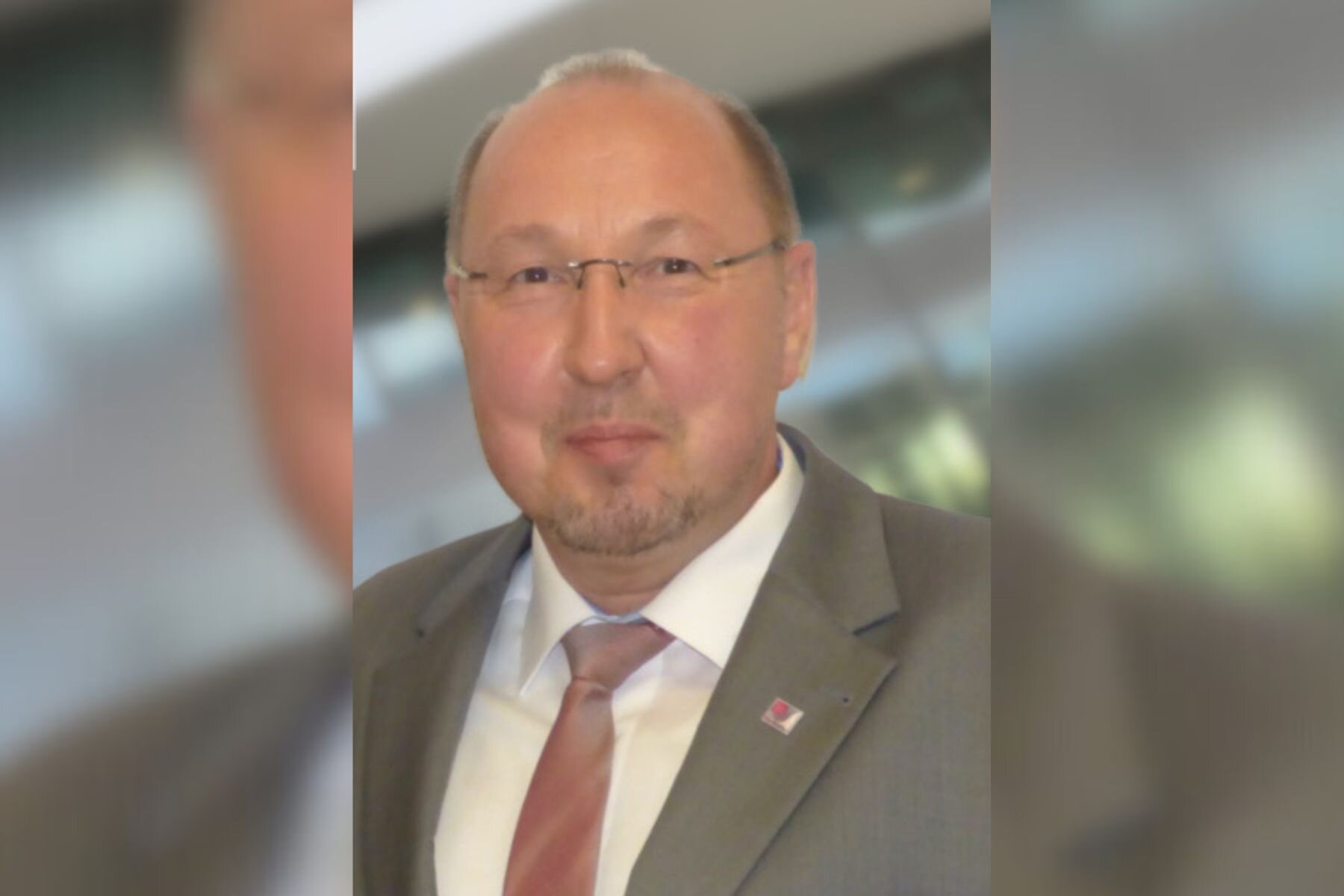 Mann mit Brille und Anzug, unscharfer Hintergrund.