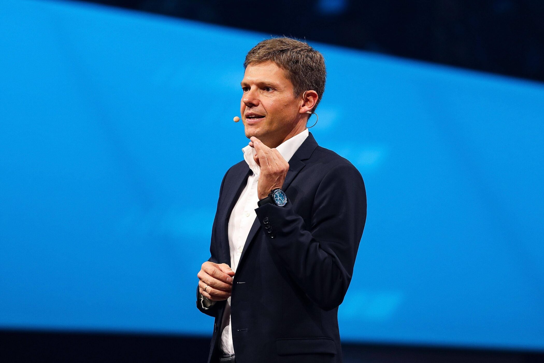 Ein Mann im Anzug spricht auf einer Bühne mit einem Headset.