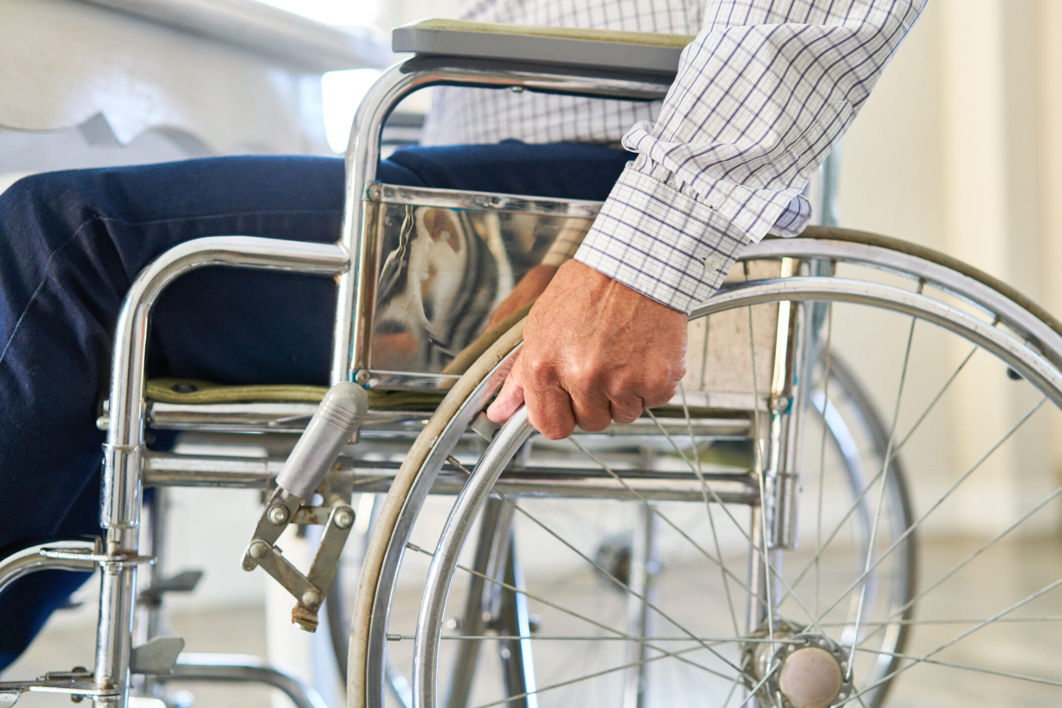 Person in Rollstuhl, Hand am Rad, kariertes Hemd.