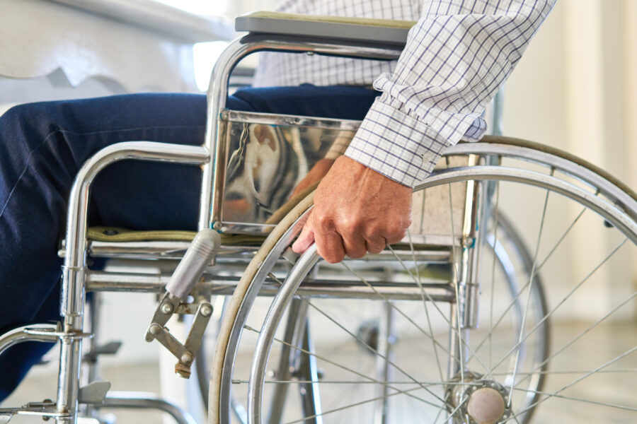 Person in Rollstuhl, Hand am Rad, kariertes Hemd.
