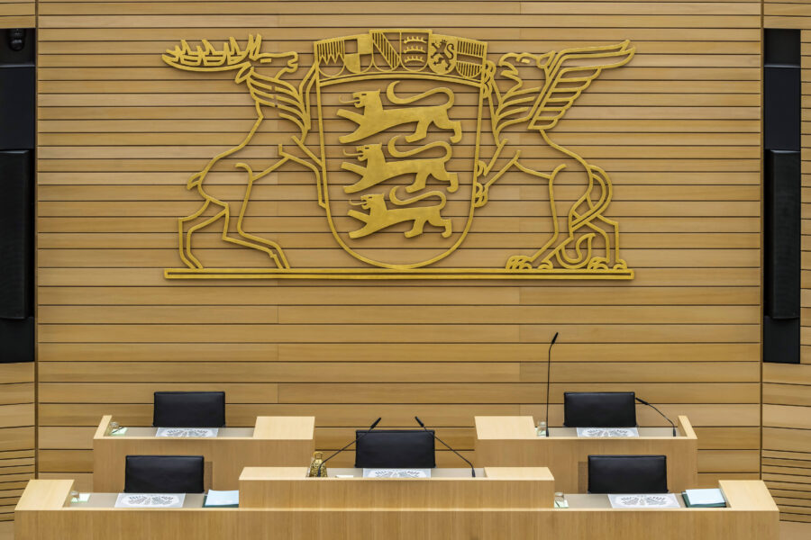 Holzwand mit Wappen und drei leeren Pulten mit Mikrofonen.