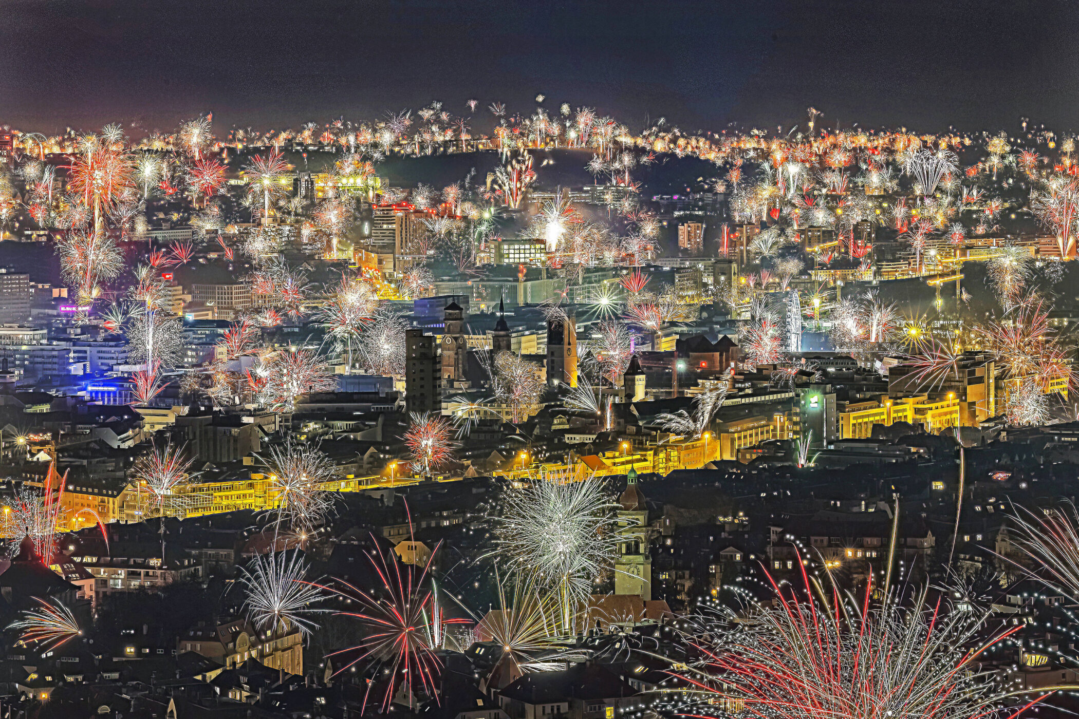 Feuerwerk über einer Stadt bei Nacht, viele bunte Lichter am Himmel.