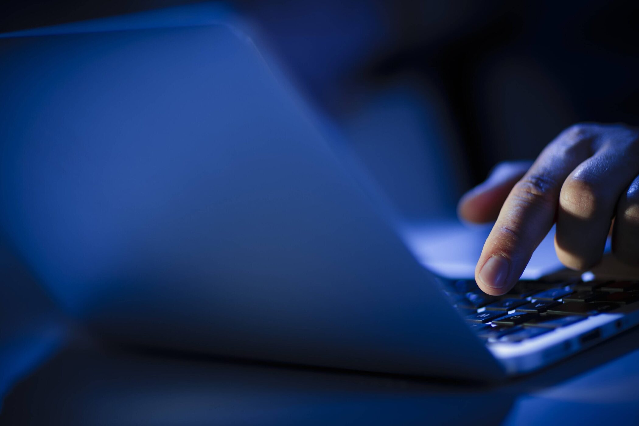 Hand tippt auf Laptop-Tastatur in blauem Licht.
