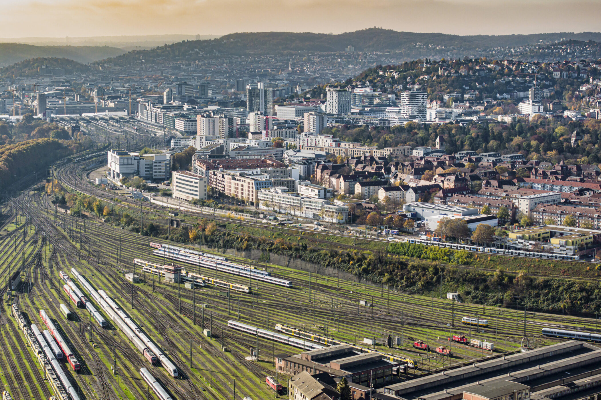 Bahnhofsgelände mit vielen Gleisen und Zügen, umgeben von Stadtgebäuden und Hügeln.