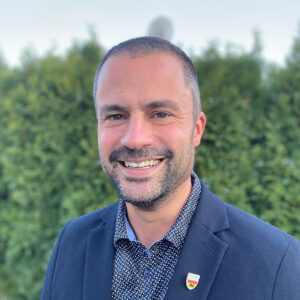 Lächelnder Mann im Anzug vor unscharfem grünem Hintergrund.