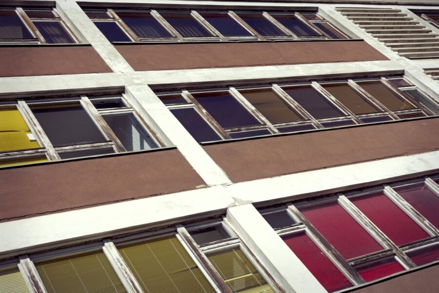 Fassade eines Gebäudes mit mehreren Fenstern und bunten Jalousien.