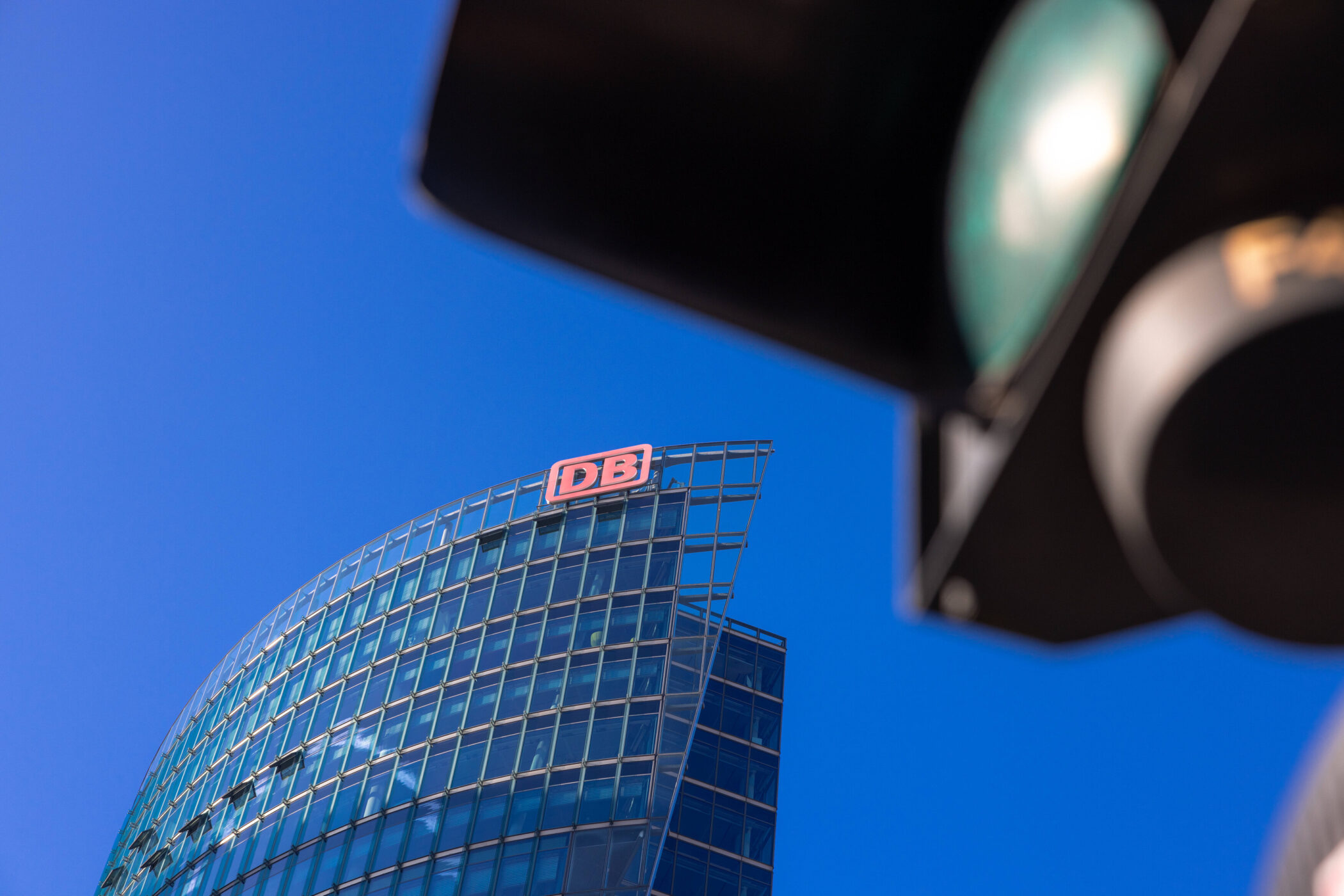 Gebäude mit DB-Logo, Ampel im Vordergrund, blauer Himmel.