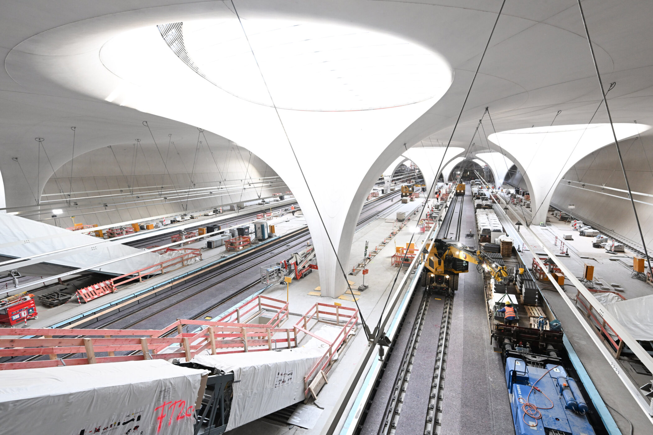 Große, moderne U-Bahn-Station im Bau mit Schienen, Maschinen und Arbeiterplattformen.