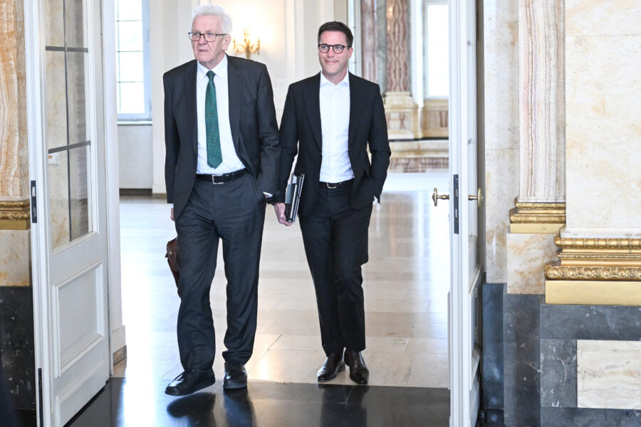 Zwei Männer in Anzügen gehen durch eine geöffnete Tür in einem eleganten Raum.