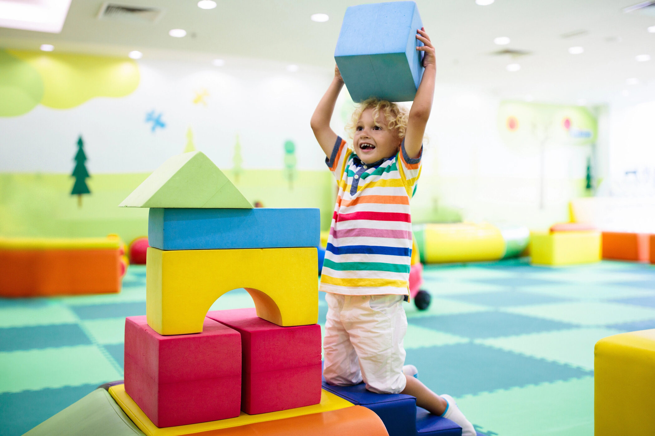 Kind in buntem Raum mit großen Schaumstoffbausteinen.