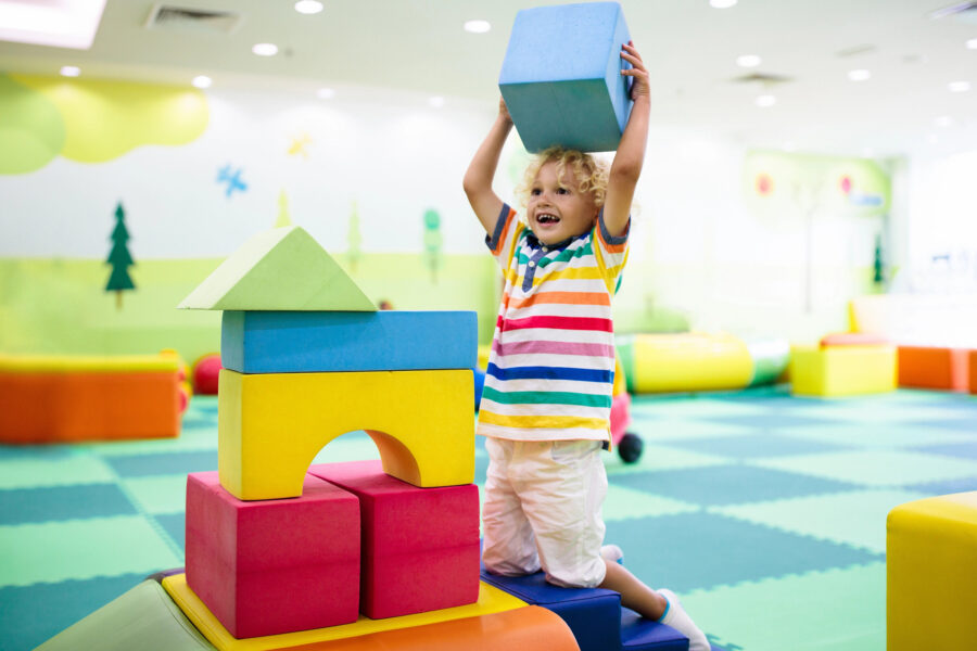 Kind in buntem Raum mit großen Schaumstoffbausteinen.