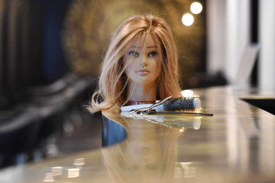 Frisierkopf mit blonden Haaren, Rundbürste und Schere auf einem Tisch.