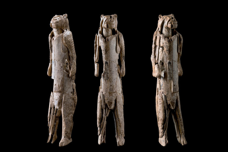 Drei geschnitzte Figuren mit tierähnlichen Köpfen auf schwarzem Hintergrund.