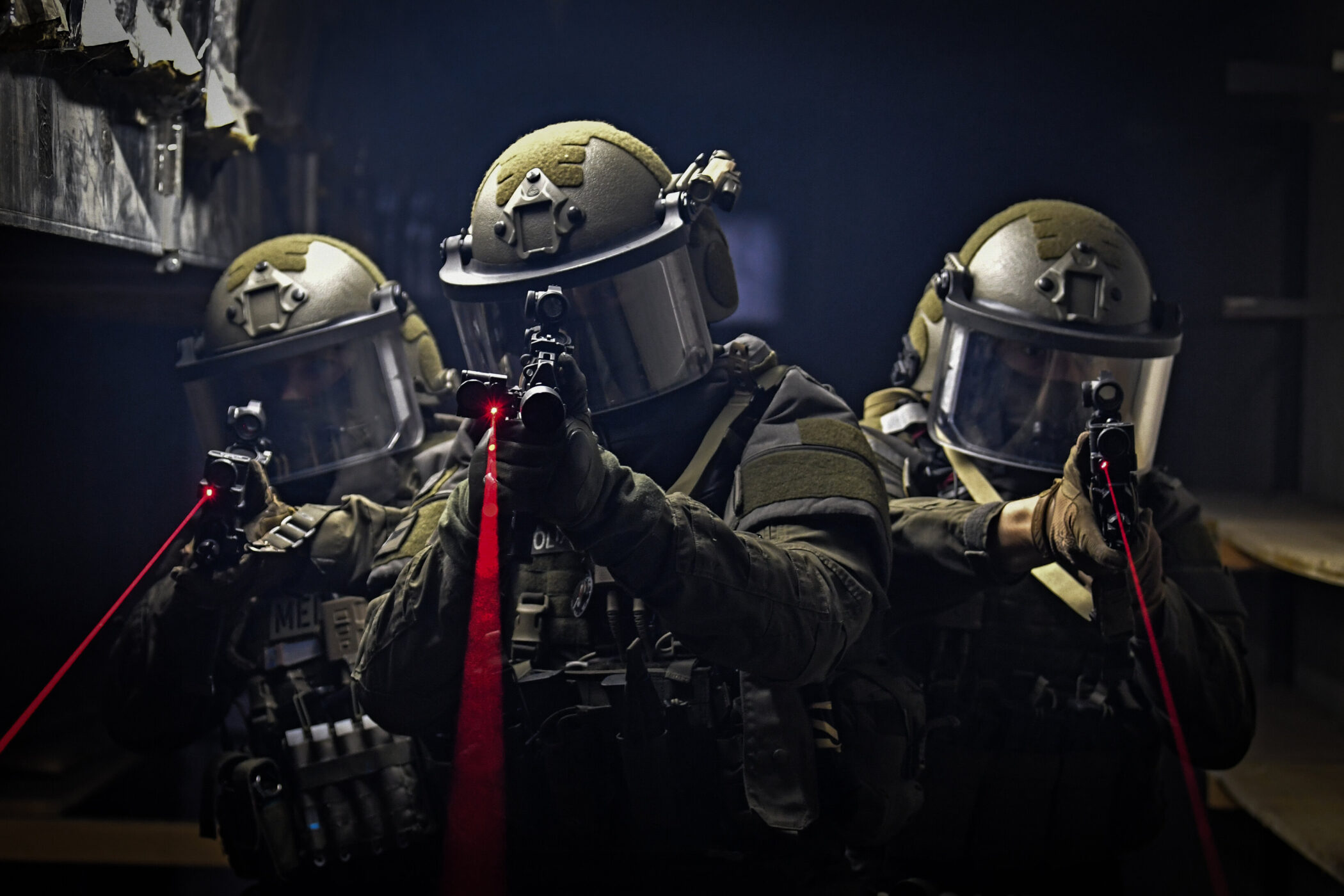 Drei Personen in Schutzanzügen mit Helmen und Laserpointern in dunkler Umgebung.