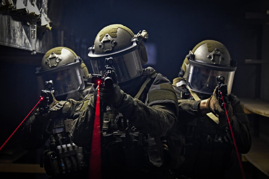 Drei Personen in Schutzanzügen mit Helmen und Laserpointern in dunkler Umgebung.