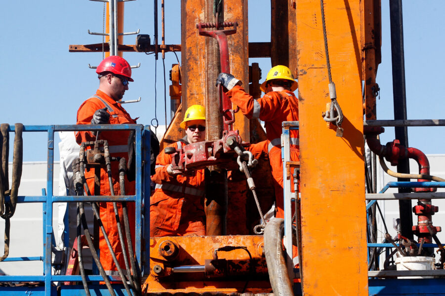 Drei Personen in Schutzkleidung arbeiten an einer Bohranlage.