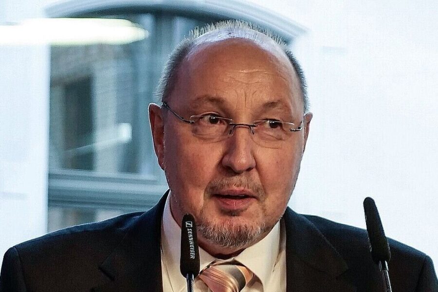 Älterer Mann mit Brille und Anzug spricht in Mikrofonen.