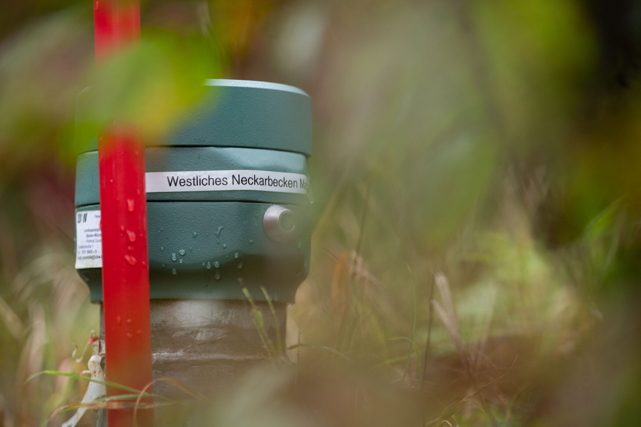 Grünes Gerät mit Aufschrift "Westliches Neckarbecken", rotes Rohr daneben, im Gras.