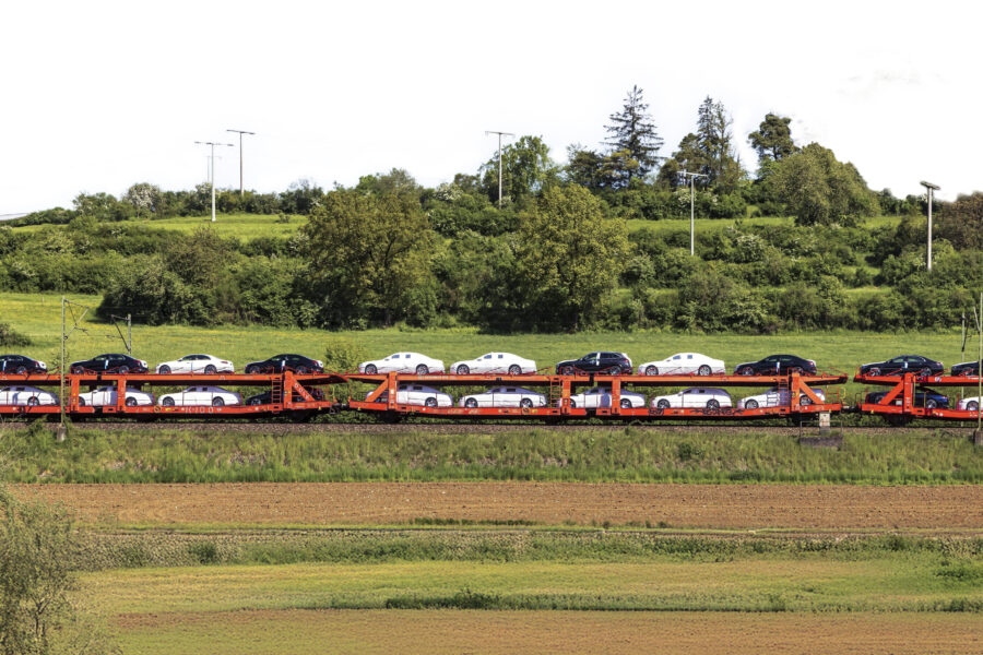 Zug transportiert Autos auf zweistöckigen Waggons durch grüne Landschaft.