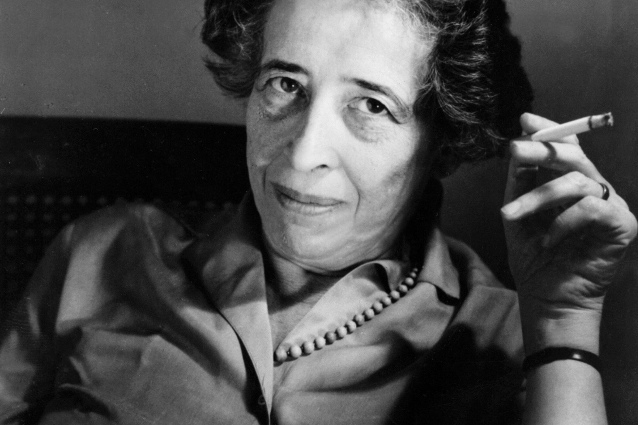 Person mit Zigarette, schaut in die Kamera, trägt eine Kette und ein Hemd.