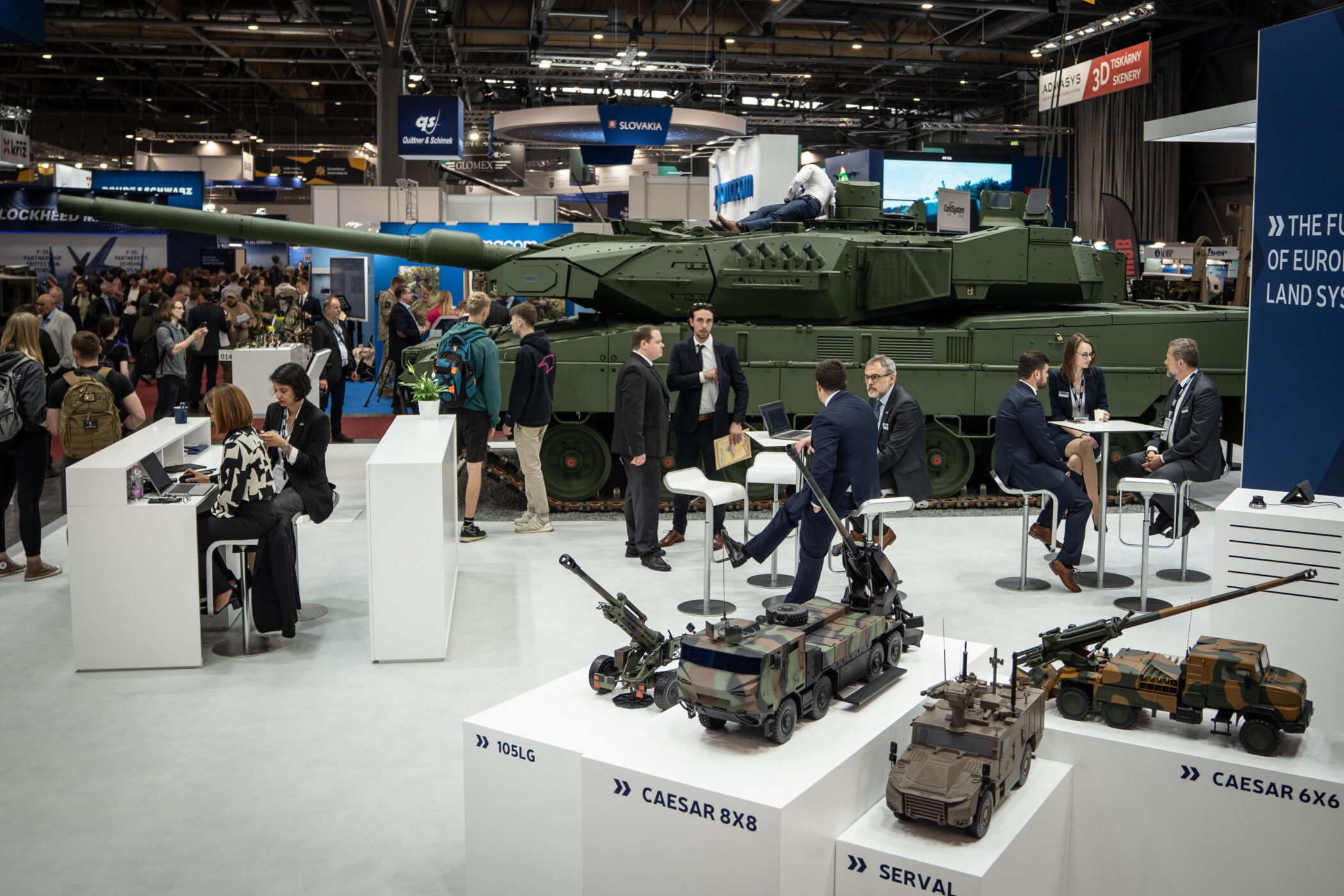 Menschen auf einer Messe, Panzer und Modelle im Hintergrund.