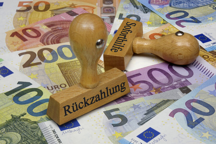 Eurobanknoten und zwei Holzstempel mit Aufschriften "Rückzahlung" und "Soforthilfe".