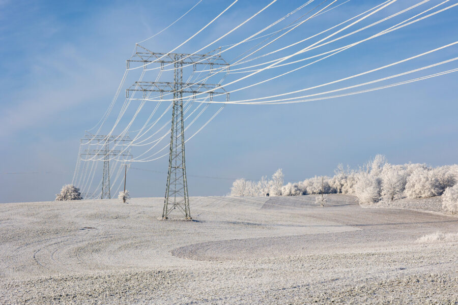 Schneebedeckte Landschaft mit Strommasten und blauen Himmel.
