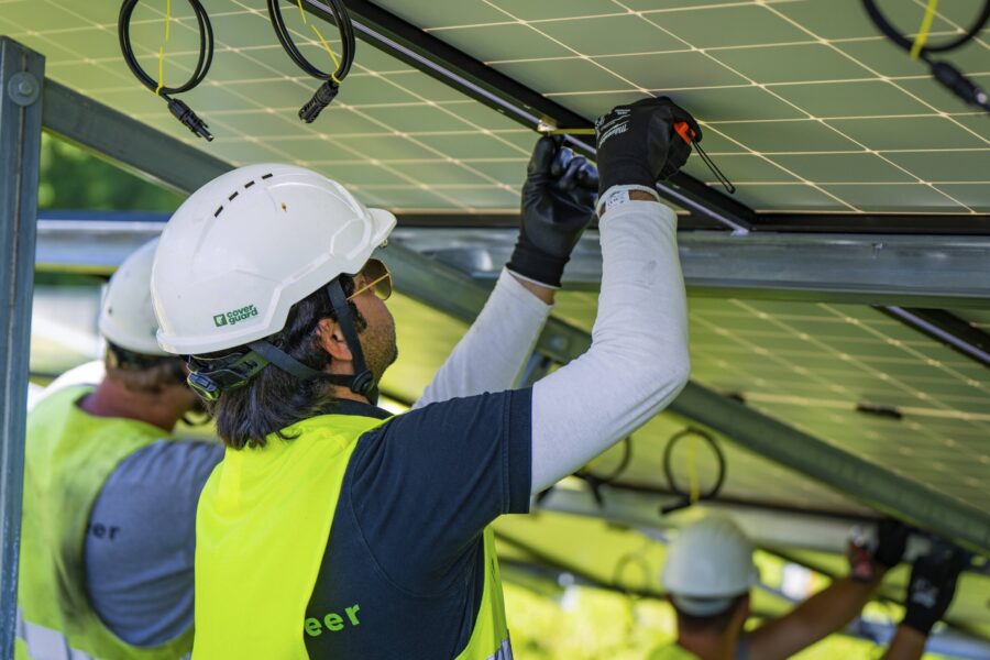 Drei Personen mit Helmen montieren Solarpanels.