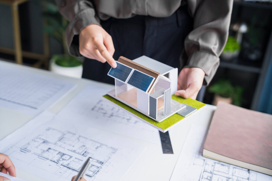 Person hält ein Architekturmodell mit Solarpanelen über Bauplänen.