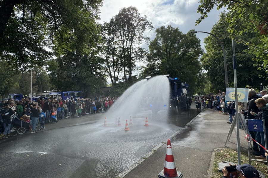 Menschenmenge beobachtet Wasserwerfer, der Wasser auf Straße spritzt.