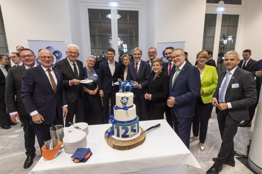 Gruppe von Menschen steht um eine dreistöckige Torte mit "125 Jahre".