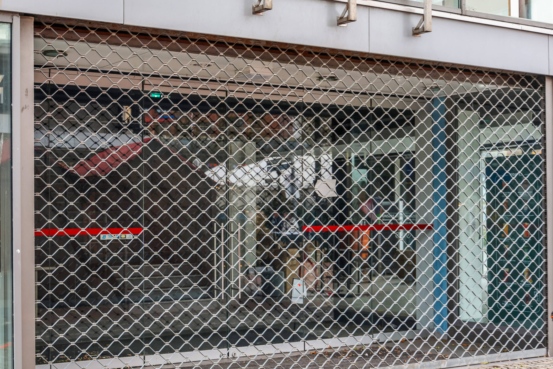Geschlossenes Rollgitter vor einem Schaufenster mit rotem Streifen.