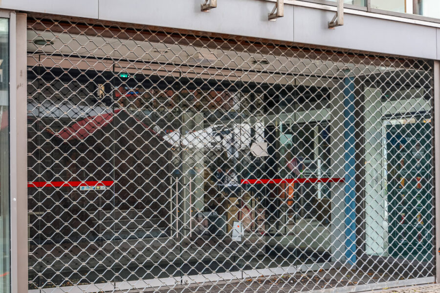 Geschlossenes Rollgitter vor einem Schaufenster mit rotem Streifen.