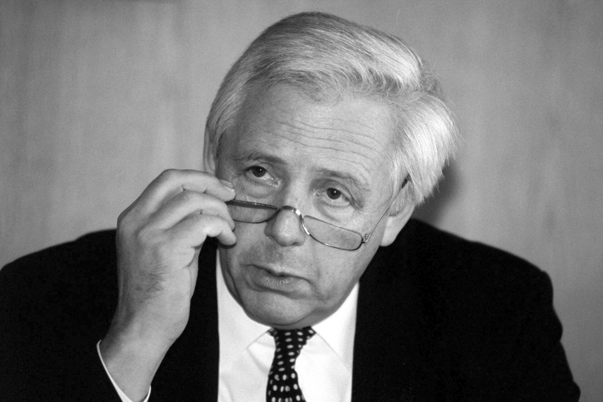 Älterer Mann mit Brille und Anzug, hebt die Brille leicht an.