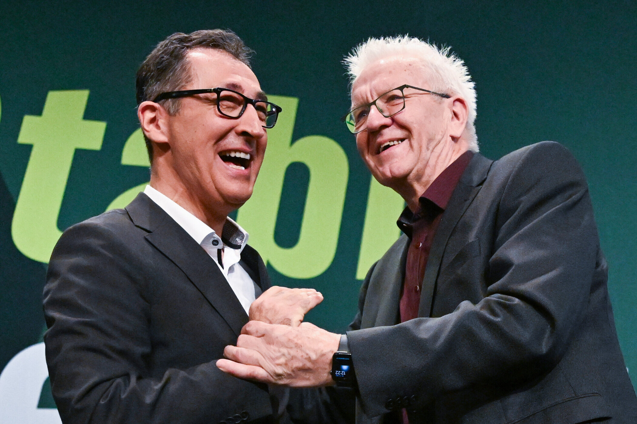 Zwei Männer in Anzügen lachen und schütteln sich die Hände.